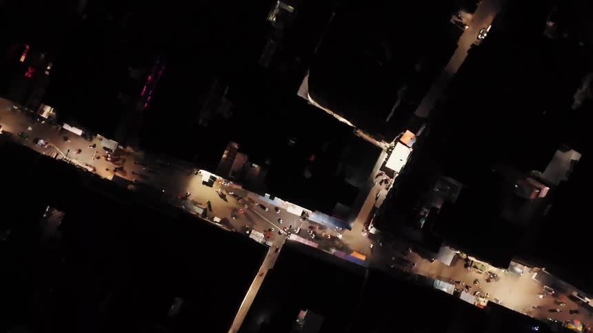 Aerial view of a city blacked out except for a lit up intersection with cars and people