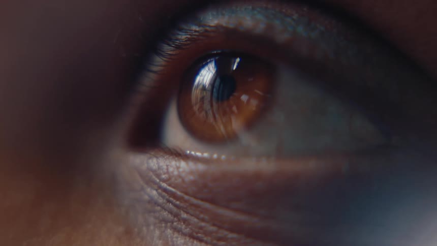 A persons eye with a brown iris that is blinking and staring straight ahead