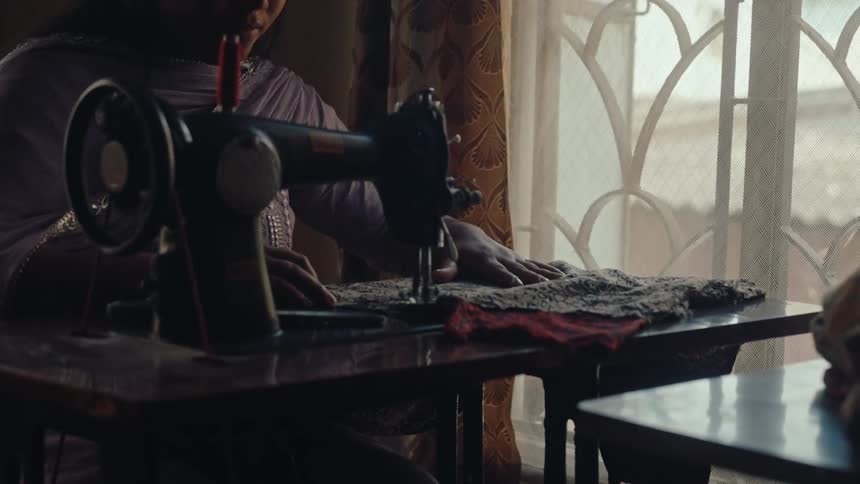 A woman sits at the sewing machine and sews a piece of clothing