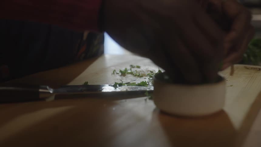 A person chopping parsley on a wooden board and placing it in a bowl