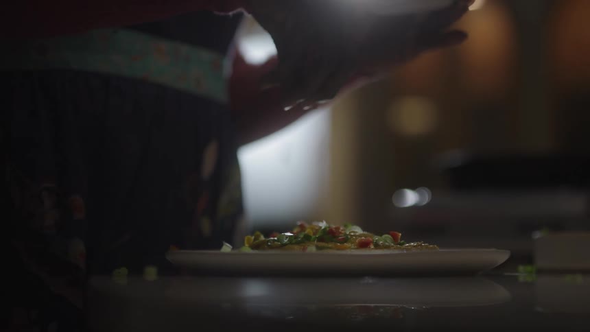 A closeup of a hand gracefully sprinkling spices over a dish in a warmly lit kitchen setting