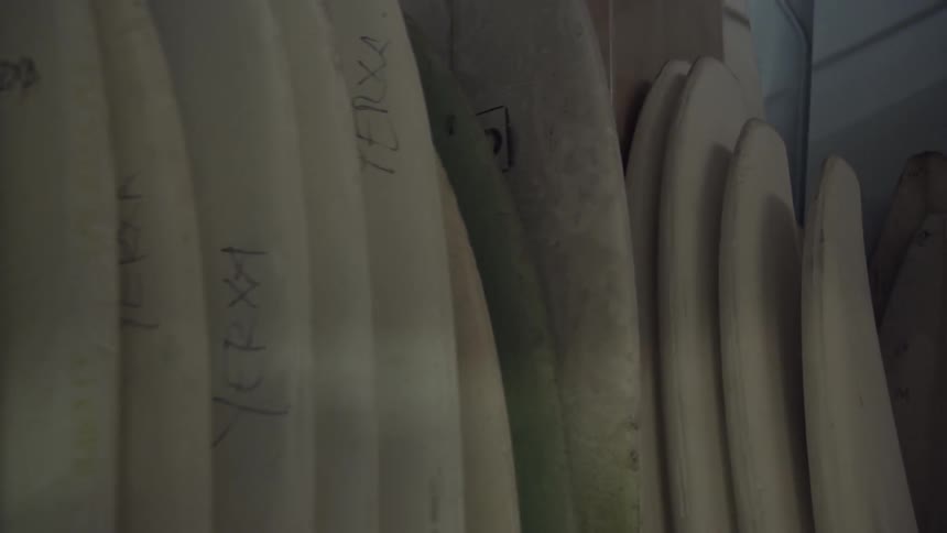 Unfinished surfboards are stacked up against a wall