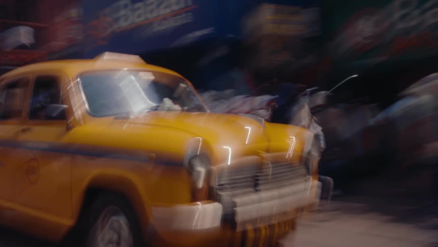 A taxi driving down a street with many people and shops on the side