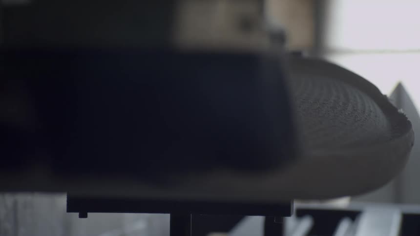 An industrial machine with a brush attached makes a pass over a surfboard