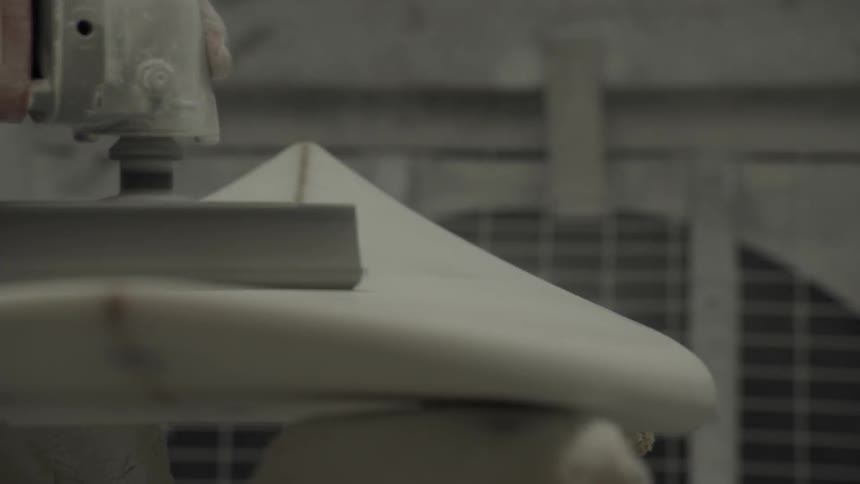 A person is using a large sander on a surfboard