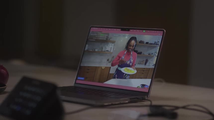 A cooking show with a woman enjoying food is playing on a video on a laptop