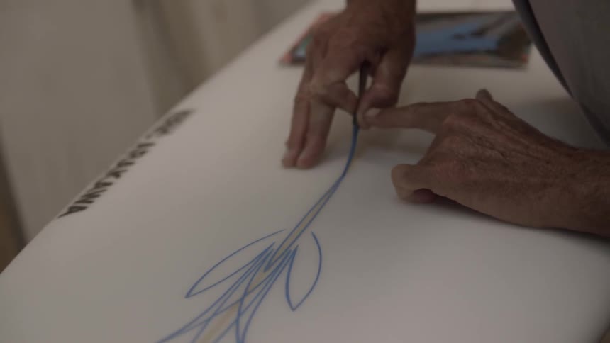 A person paints a decoration on a surfboard