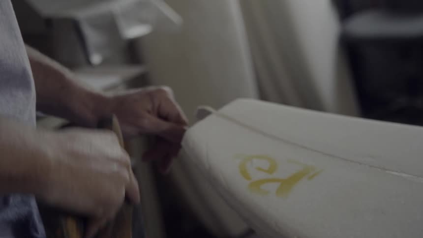 A man is sawing the edge of a surf board
