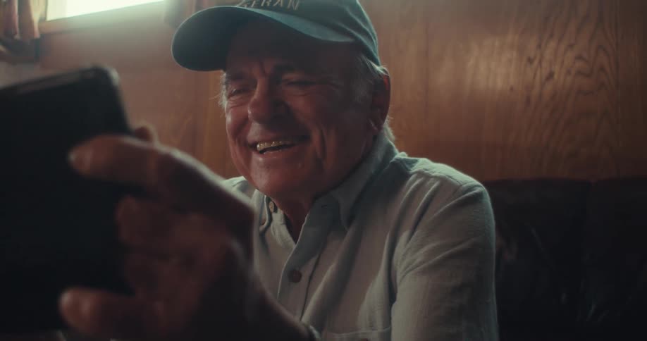 Elderly man in cap interacting with tablet and laughing