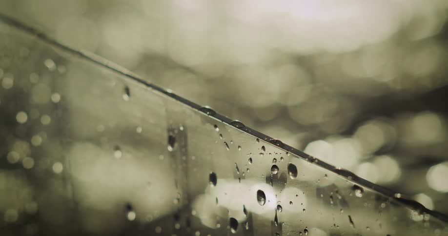 A closeup shot of water droplets sliding down a pane of glass with a softly blurred golden background