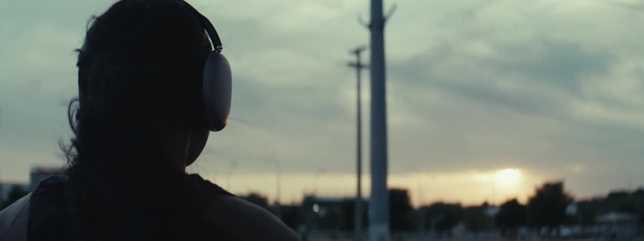 A teenage girl wearing headphones is shown from behind watching a sports game on the field