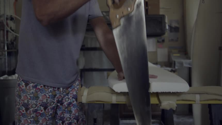 A man is using a saw to trim off the ends of a surfboard