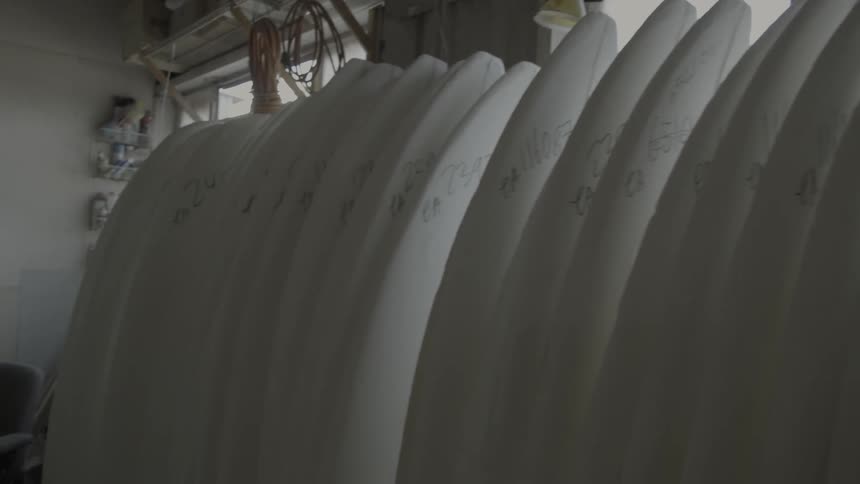 Unfinished surfboards are stacked next to a window