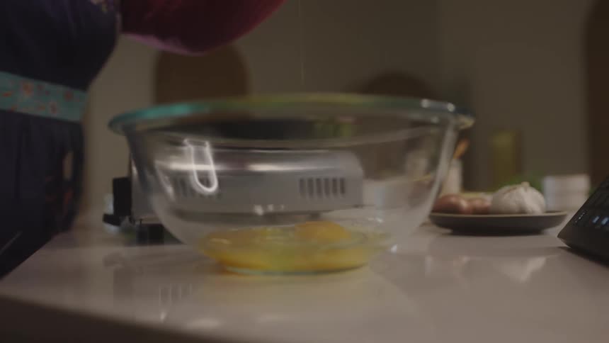 Black woman cracks and pours egg contents into a bowl