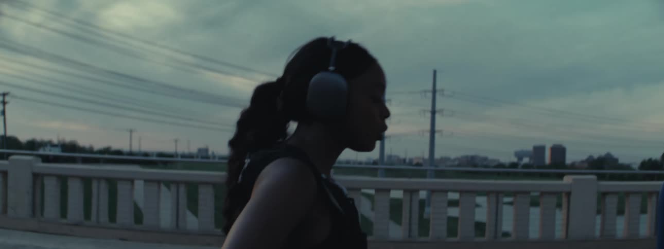 Woman wearing headphones running on a bridge then stopping to rest