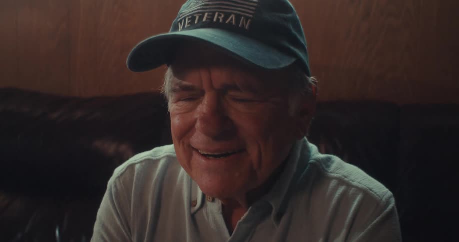 An elderly man wearing a veteran hat sitting and smiling
