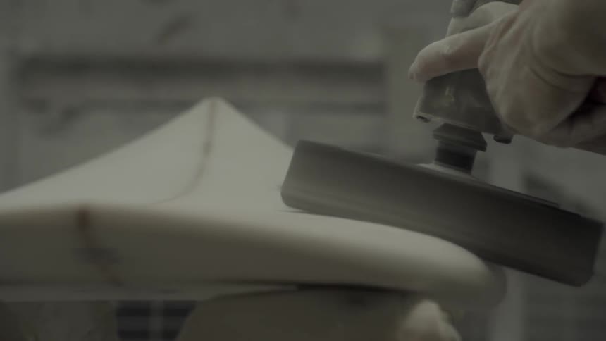 A worker uses a sander to smooth an unfinished surfboard