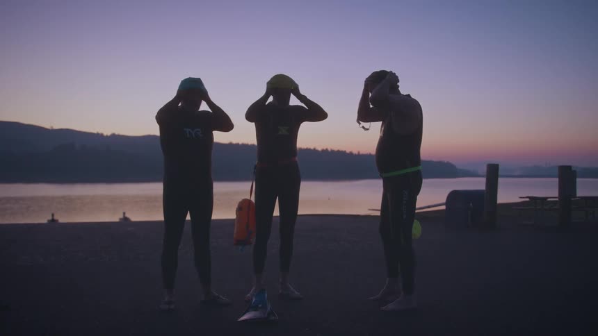 Three men putting on swimming caps by a lake on a sunrise in their purple