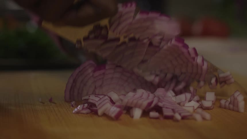 Pair of gloved hands cutting a red onion with a knife
