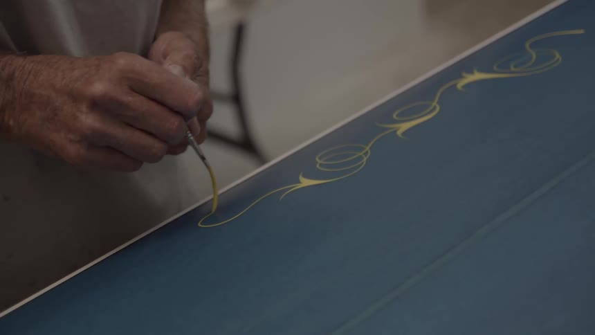 A man is using a brush to paint a design on a surfboard