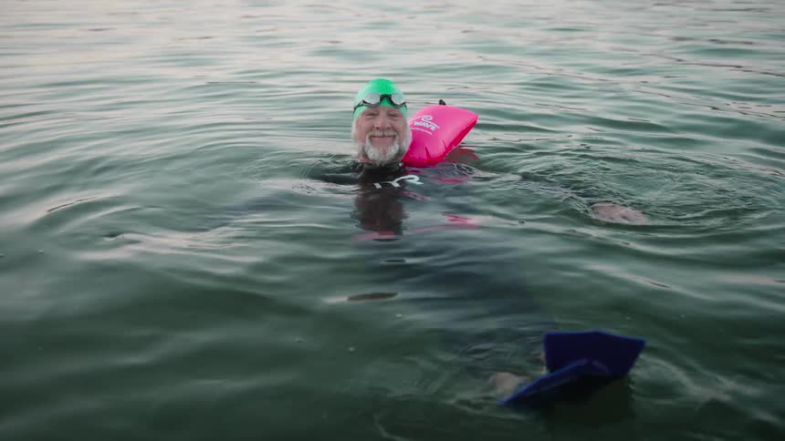 Older man floating in the water with diving equipment swim goggles and swim fins