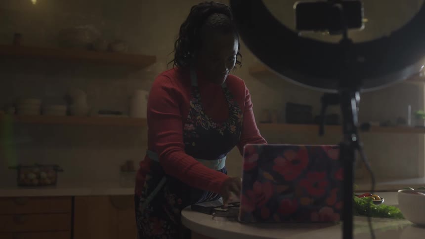 A woman setting up her laptop in the kitchen with a ring light positioned in front of her as she prepares for an online cooking session