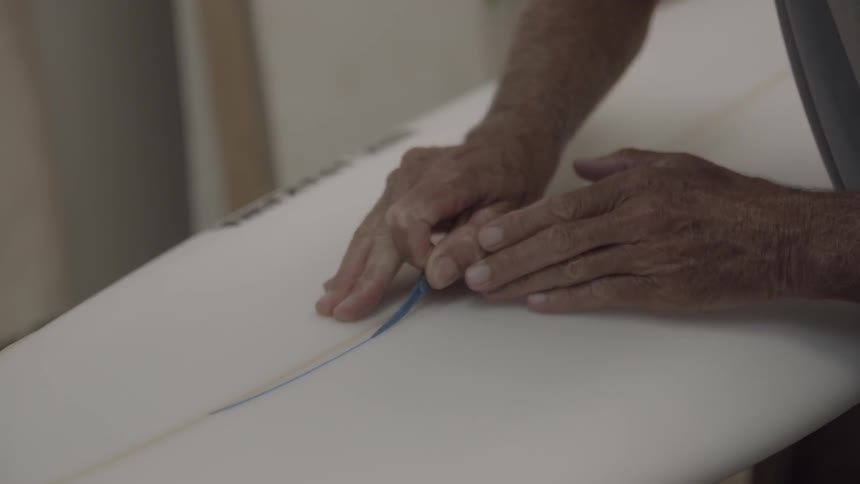 A man is using a brush to paint a thin line on a surfboard