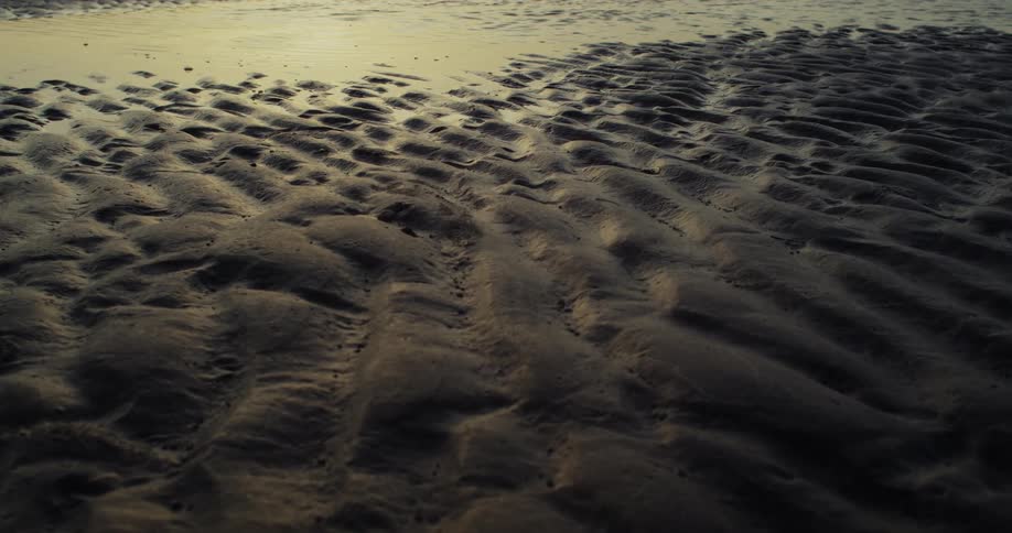 Aerial shot of rippled sand at low tide with water in the background taken during golden hour