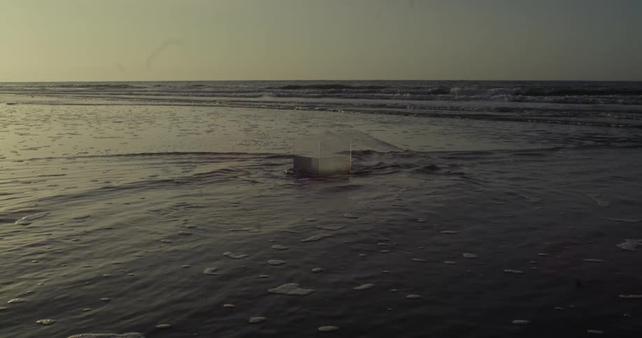 Ocean water flowing on the beach around a glass cube half filled with water