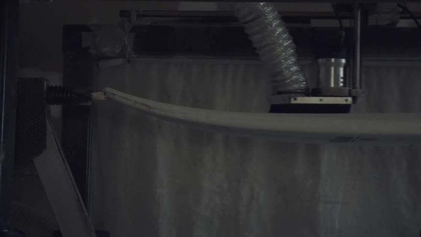 An industrial machine with a brush attached makes a pass over a surfboard