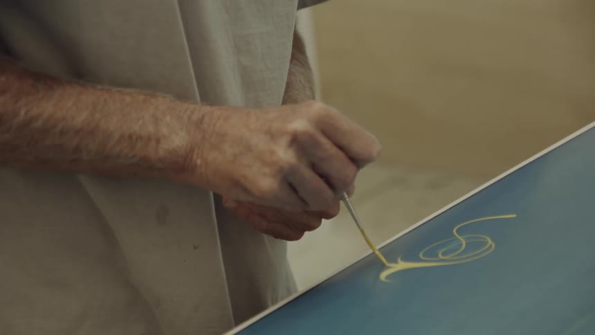A man is using a brush to paint a design on a surfboard