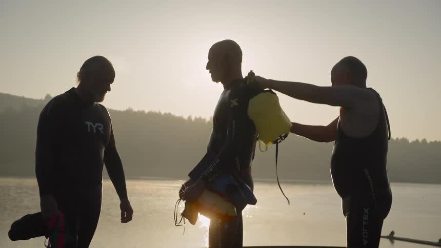 Three men preparing to dive one of them helping the other get dressed