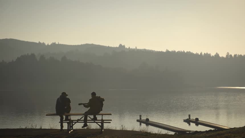 A man plays guitar by the lake as it rains