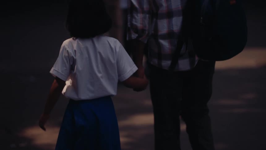 Father and daughter hold hands as they walk down a busy street