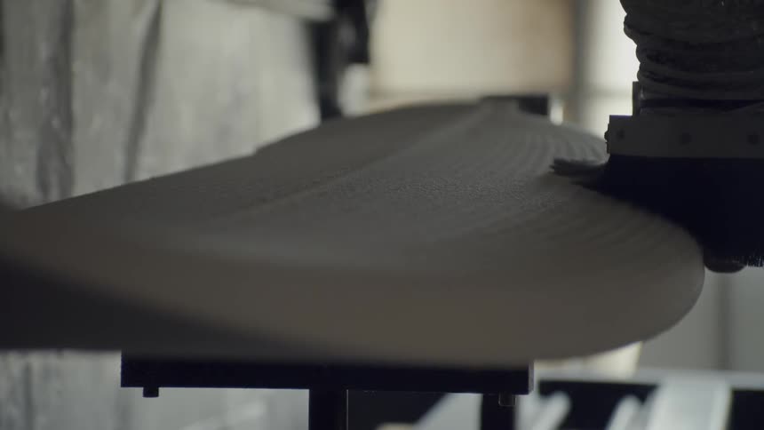 A person uses a tool on an unfinished surfboard