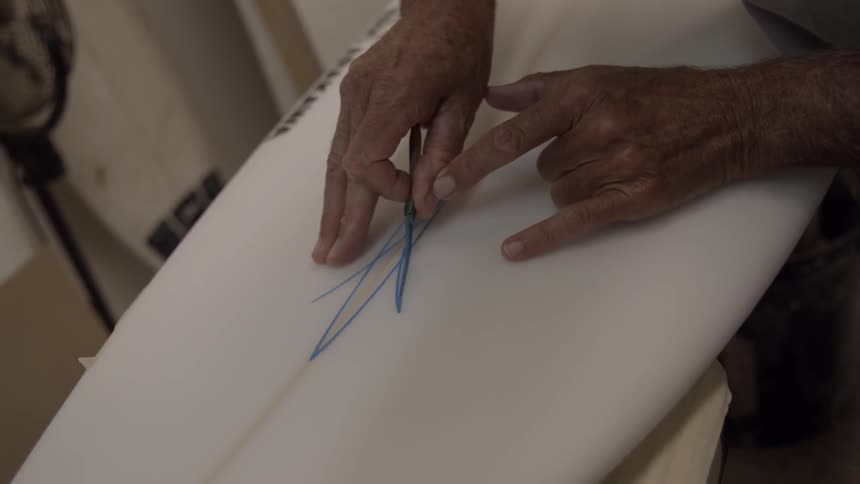 A person paints a design on a surfboard