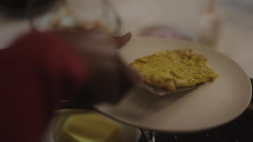 Woman takes a cooked omelette out of a pan and places it on a plate