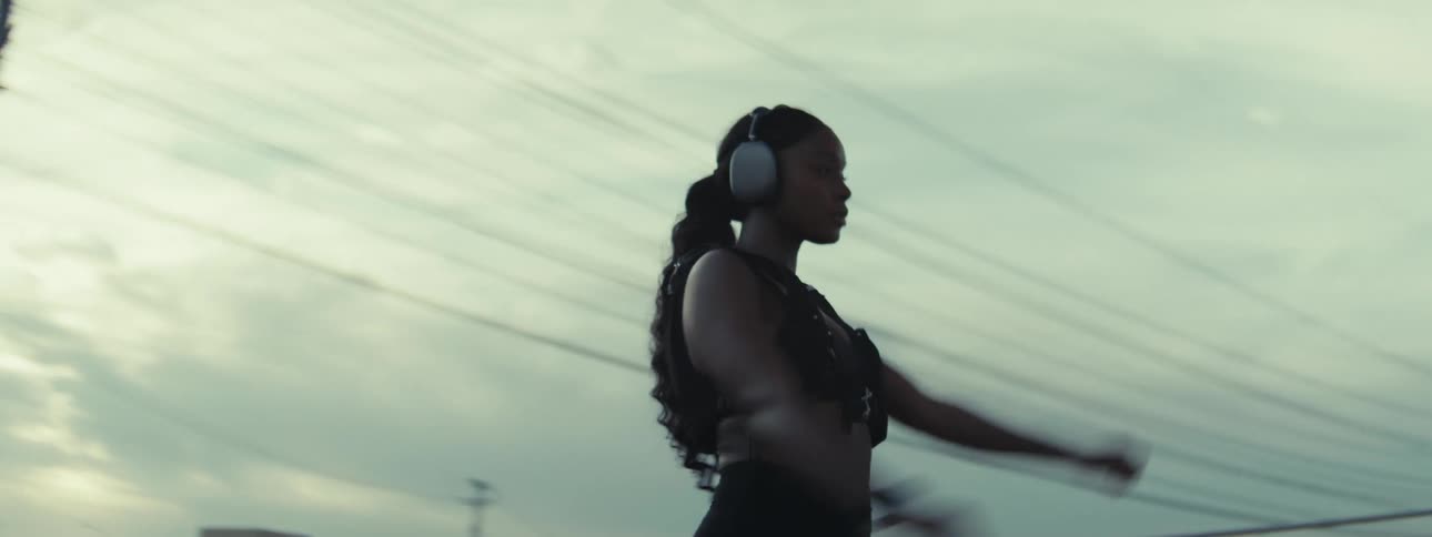 Woman wearing headphones stretches while standing outdoors on a cloudy day