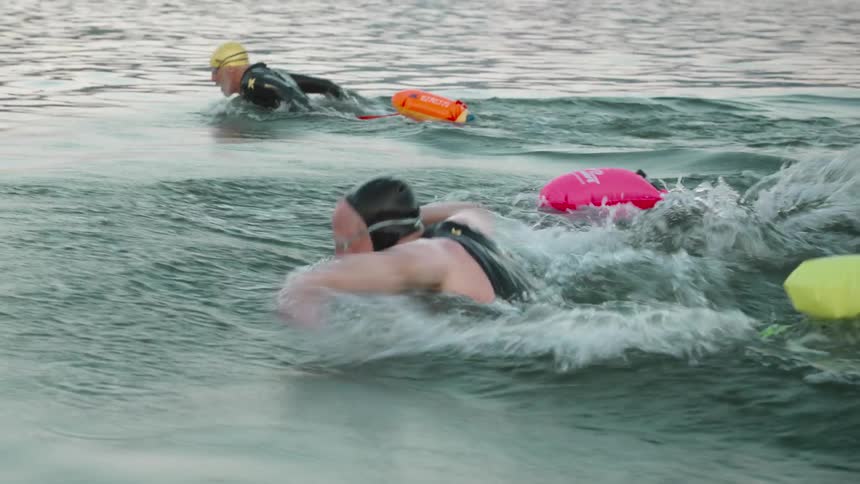 Three men with balloon tags swimming in the lake at daytime