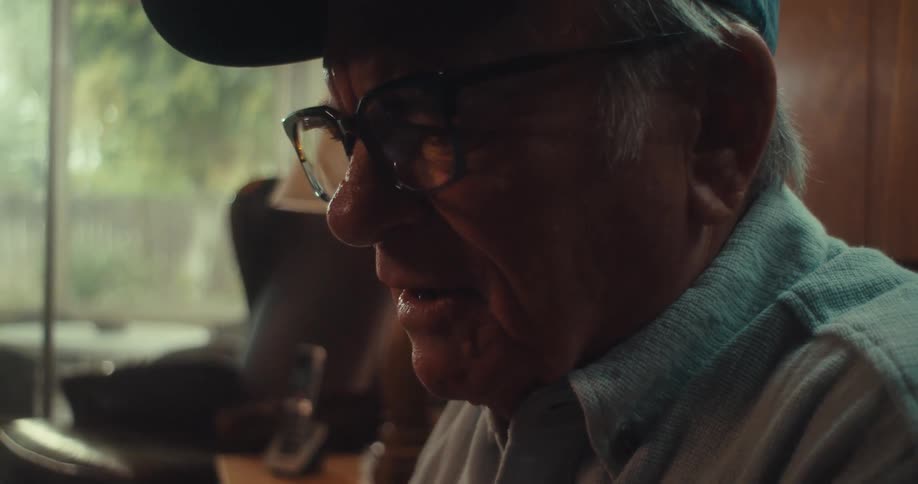 An elderly man sitting on the living room sofa watching a game on his tablet and cheering