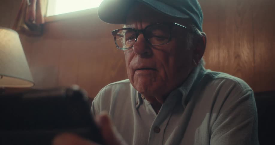 Elderly man sitting in his living room focuses on a tablet
