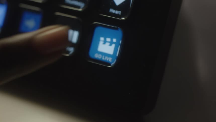 A persons finger pressing a button labeled go live on an electronic device with several other buttons