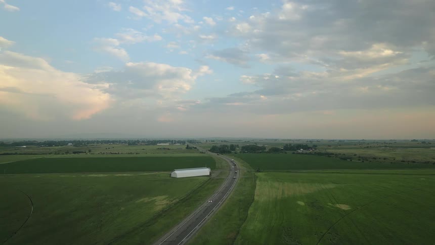 Aerial view of a long highway surrounded by green and agricultural fields