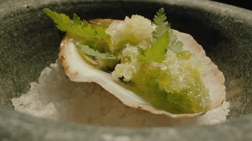 Tweezers gently placing herbs on a plate in a ladle in a ceramic bowl