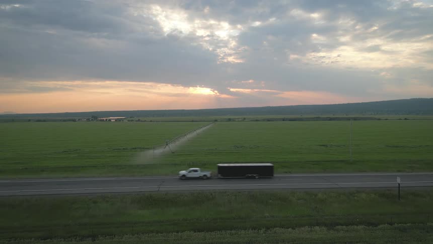 Vehicles driving across rural road in the country as the sun rises in the distance