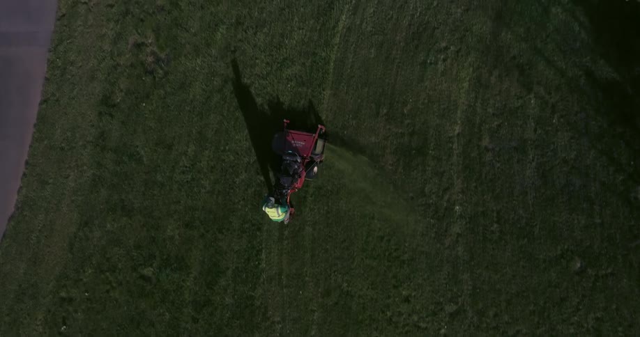 A topdown aerial view captures a person mowing a vibrant green grass field