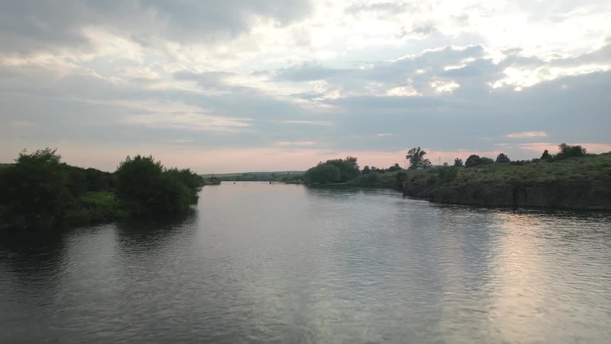 A serene river flows between lush green banks under a cloudy sky with hints of sunlight breaking through