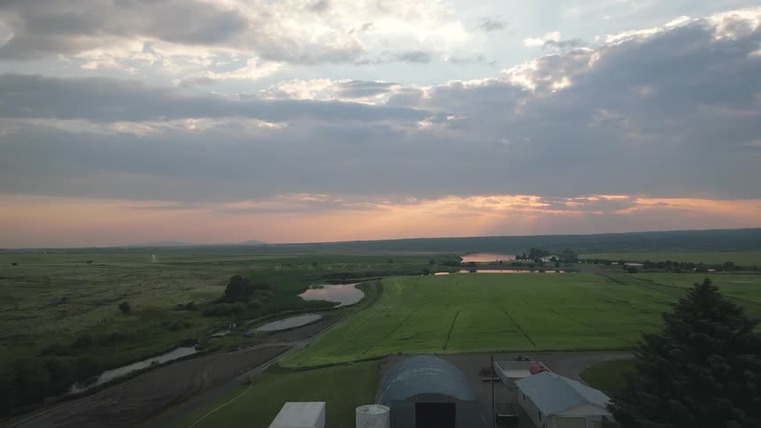 A scenic aerial view of a farm with fields trees and a house under a cloudy sunset sky