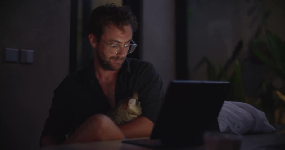 Man in front of a laptop with a cat on his lap