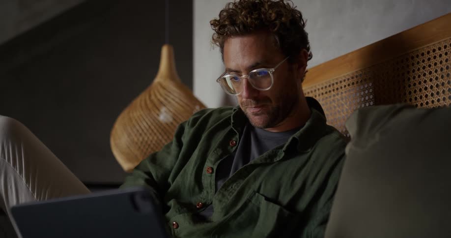Man uses a tablet device on a bed in a room